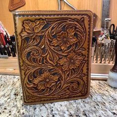 an intricately carved leather wallet sitting on top of a counter next to scissors and other office supplies