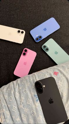 four different colored iphones sitting next to each other on top of a bed,