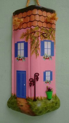 a pink house with blue doors and windows hanging on the side of a white wall