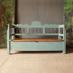 a blue bench sitting in front of a wall with trees on the walls behind it