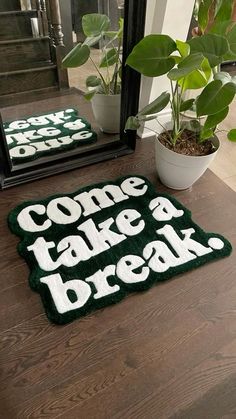 a green door mat that says come take a break next to a potted plant