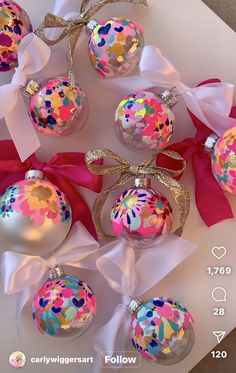 christmas ornaments with ribbons and bows are on a white tablecloth, next to a pink ribbon