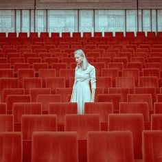 a woman standing in the middle of a room filled with red chairs