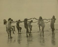 a group of people standing on top of a beach next to the ocean holding hands