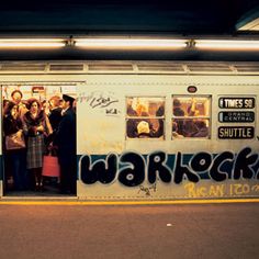 some people are standing in the doorway of a subway car with graffiti on it's side