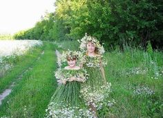 two people standing in the grass with flowers on their heads