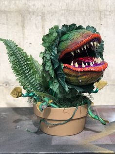 a fake dinosaur head in a potted plant with green leaves on the side and teeth