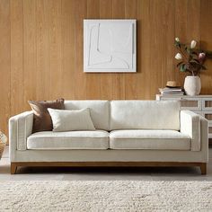 a white couch sitting in front of a wooden wall next to a vase with flowers