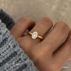 a woman's hand wearing a gold ring with a round diamond on the middle