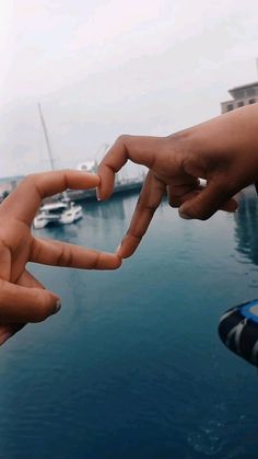 two hands reaching out towards each other over water with boats in the backgroud