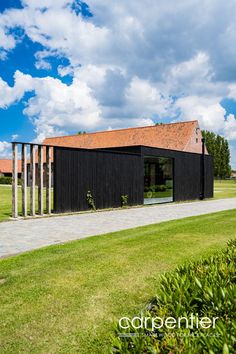 a black building sitting in the middle of a lush green field under a blue sky with white clouds