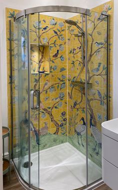 a bathroom with yellow and blue wallpaper, glass shower stall and white sink area