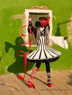 a woman dressed in black and white is holding a red ribbon while standing next to a green wall