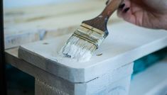 a person holding a paint brush over a white box with wood trimming on it