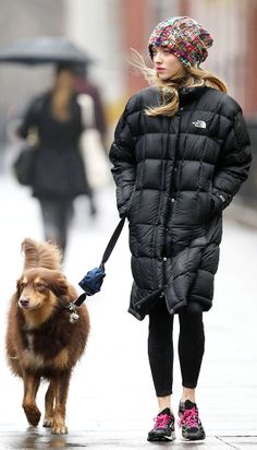 a woman is walking her dog down the street with an umbrella over her head and she's wearing a black puffy coat