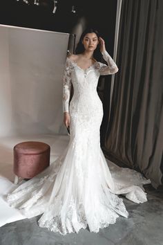 a woman in a white wedding dress standing next to a gray chair and grey curtain