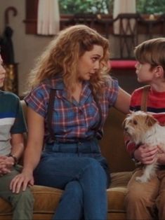 three people sitting on a couch with a dog in front of them and one person holding a small white dog