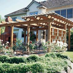 an outdoor patio with wooden pergols and flowers on the ground in front of a house