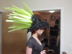 a woman wearing a dragon hat with green feathers on it's head in front of a mirror