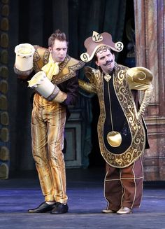 two men dressed in costumes on stage with one holding a jug and the other wearing a hat