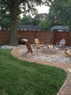 an outdoor fire pit surrounded by lawn chairs and graveled area with trees in the background