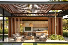 an outdoor kitchen and dining area with wood slats on the roof, surrounded by grass