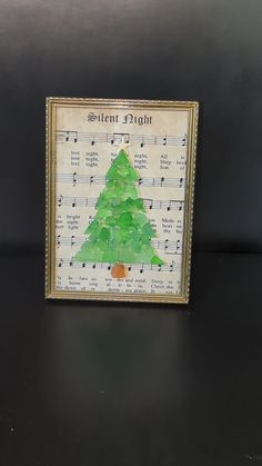 a christmas tree made out of sheet music is displayed in a frame on a table