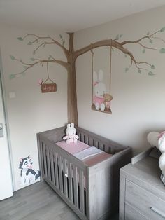 a baby's room with a tree painted on the wall and stuffed animals in the crib