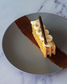 a piece of cake with bananas and chocolate on it sitting on a plate next to a marble counter top