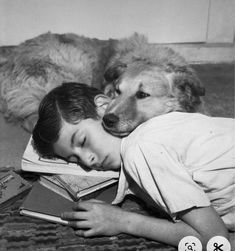 a young boy laying on the floor next to a dog with his head on a book