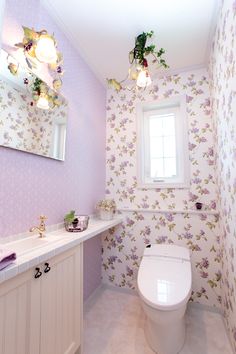 a white toilet sitting in a bathroom next to a sink under a window with purple flowers on it