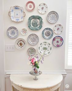 a vase with flowers sitting on top of a table next to plates hanging on the wall