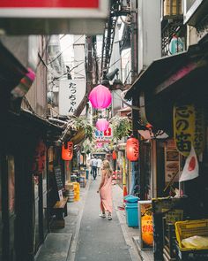 a woman in a pink dress walking down an alley way with lanterns hanging from the ceiling