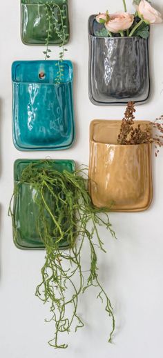 four different colored vases with flowers in them on the wall next to each other