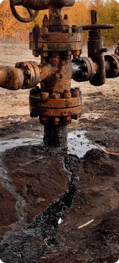 an old rusty pipe with water coming out of it's sides and some rust on the ground