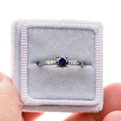 a person holding a ring with a blue stone in it's center and two diamonds on the band