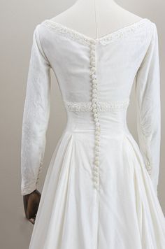 the back of a white wedding dress with buttons and pearls on it's shoulders