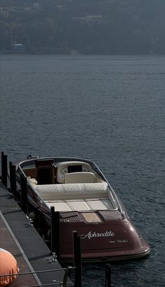 a boat docked at the end of a pier with another boat in the water behind it