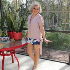 an older woman standing in front of a patio table with potted plants on it