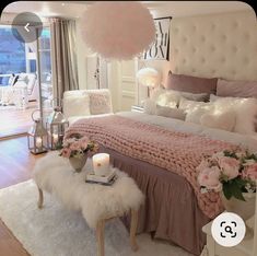 a bedroom decorated in pink and white with flowers on the bed, lights hanging from the ceiling