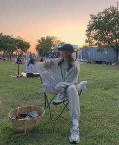 a woman sitting in a chair on top of a grass field next to a basket