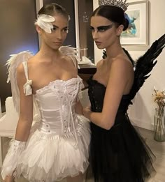 two beautiful women standing next to each other in dresses with feathers on their head and one wearing a tiara