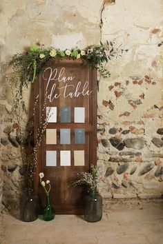 a wooden sign with flowers and greenery on it next to two vases filled with flowers