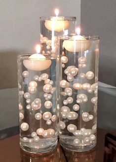 two glass vases filled with pearls and lit candles