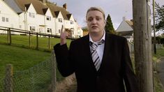 a woman wearing a suit and tie standing next to a fence with houses in the background