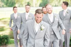 a group of men standing next to each other wearing grey suits and white flowers in their hair