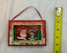 a christmas ornament hanging on a wall next to a ruler