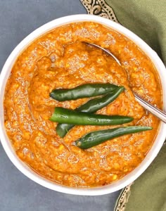 a white bowl filled with chili and green beans next to a spoon on top of a table