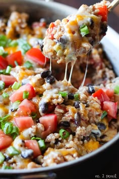 a spoon full of mexican rice with black beans, tomatoes and green onions on it