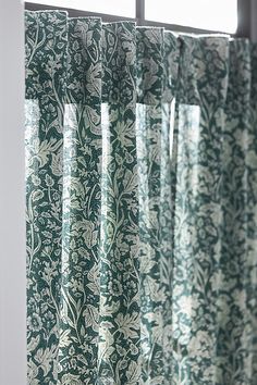 the curtain is hanging in front of the window with green and white floral designs on it